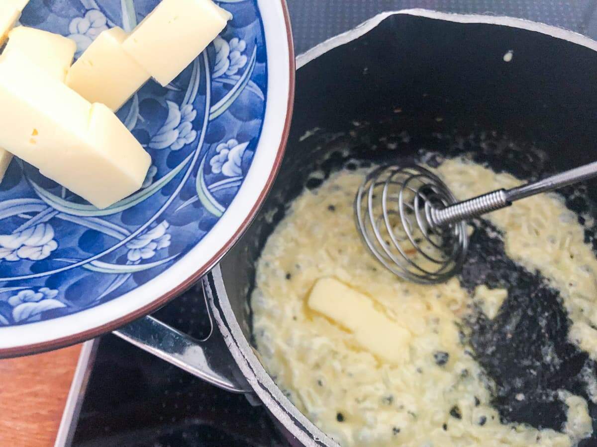 Butter cubed and being added to a fry pan of cooked soft onion to finish the process of making a butter sauce.