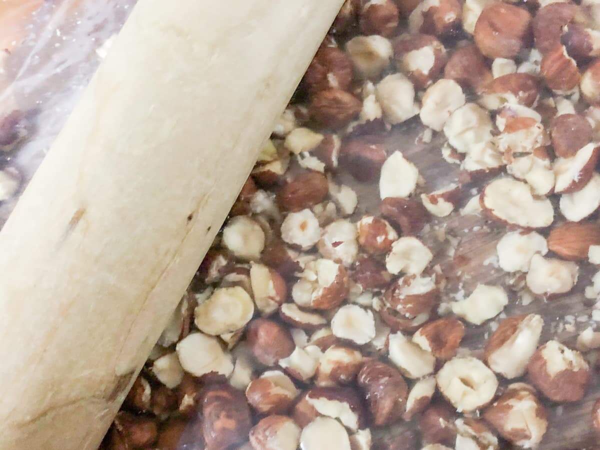 Crushing hazelnuts in a plastic bag with a rolling pin.