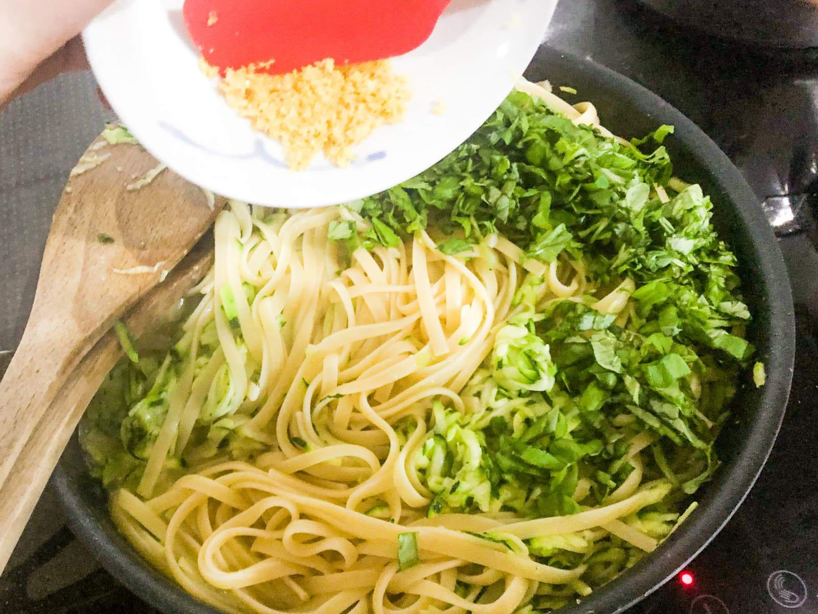 Cooked pasta being tossed with grated courgettes (zucchini) and parmesan cheese and lemon zest being added