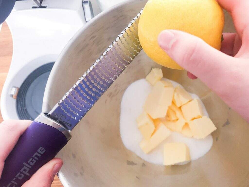 Butter and sugar in a bowl and adding in lemon zest to prepare lemon butter biscuits.