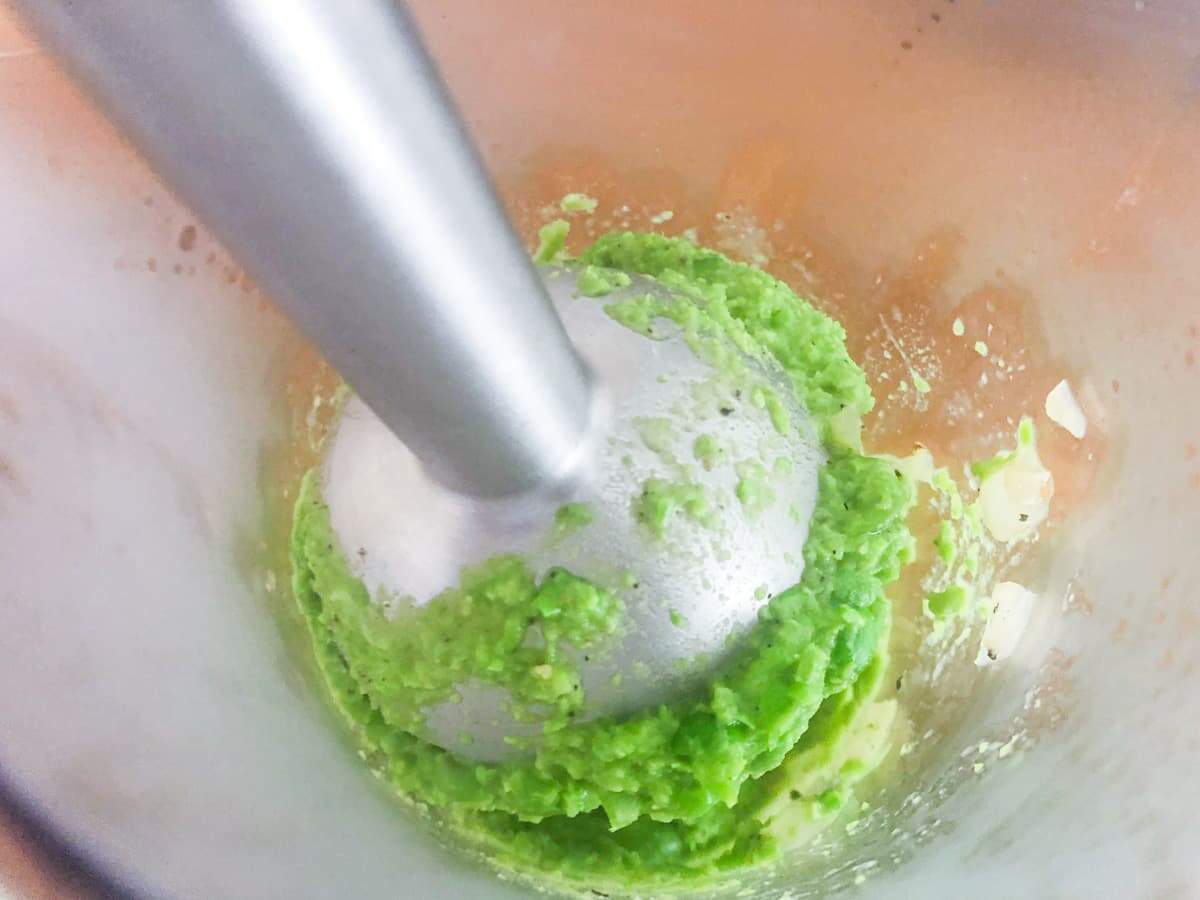 A pea puree being blended with a stick blender