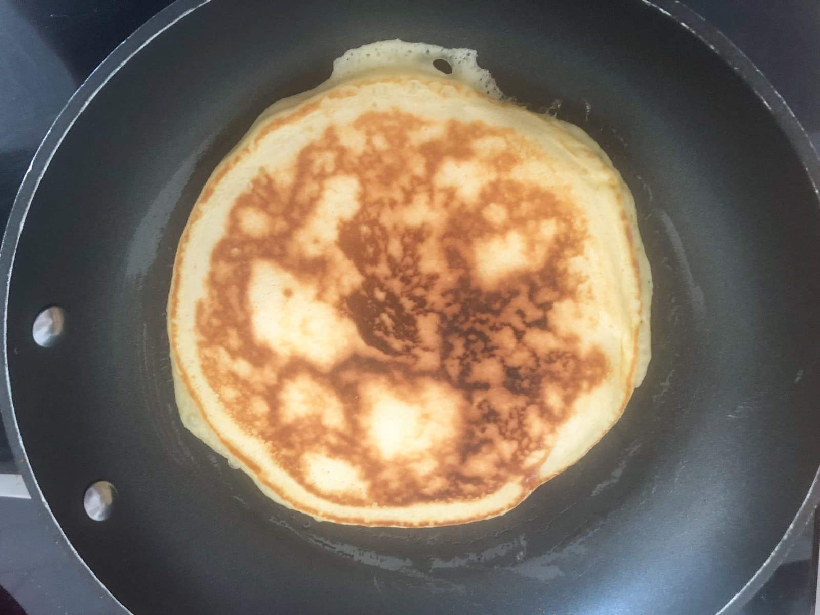 A scotch pancake flipped over showing the caramelisation on the pancake after one side was cooked.