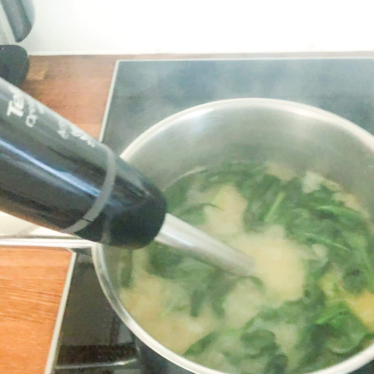 Wild garlic soup cooking in a pan on the stove and being blended with a stick blender