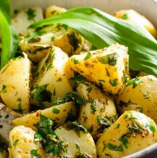 A delicious looking warm wild garlic potato salad in a mottled blue and white ceramic bowl on a dark blue waffled tablecloth.