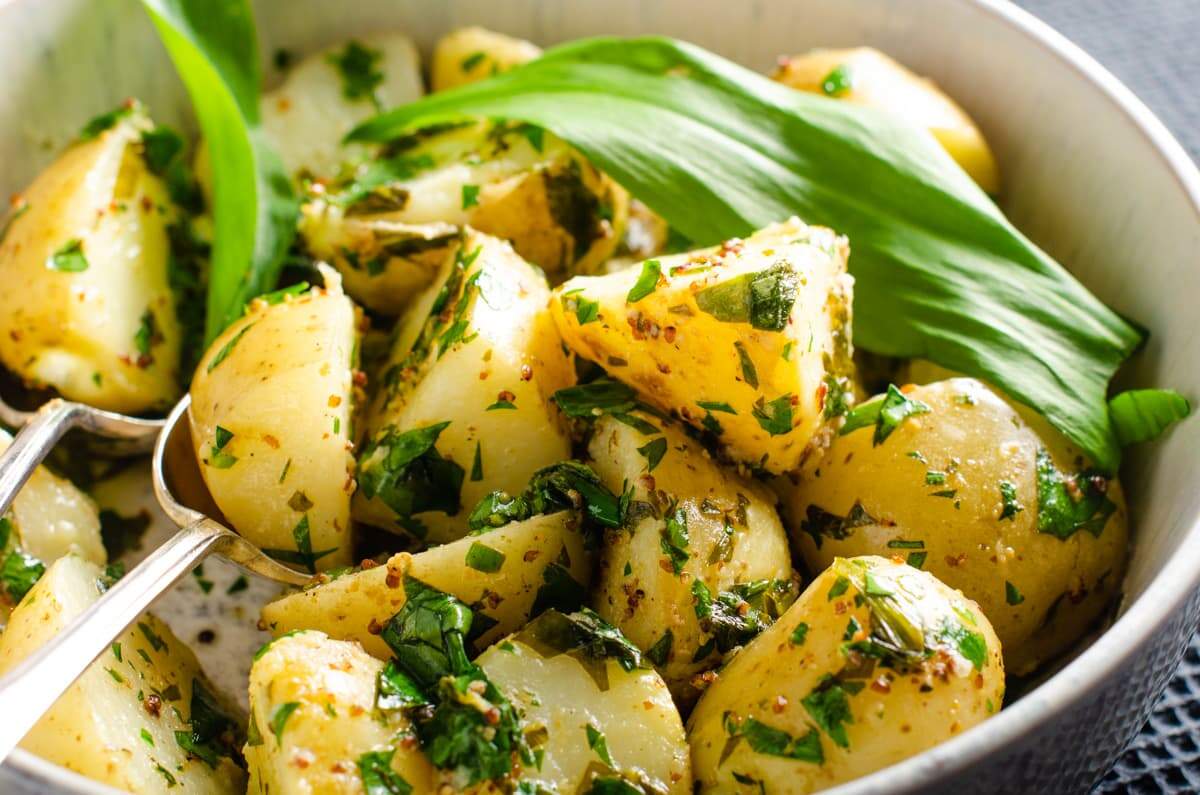 A delicious looking warm wild garlic potato salad in a mottled blue and white ceramic bowl on a dark blue waffled tablecloth.