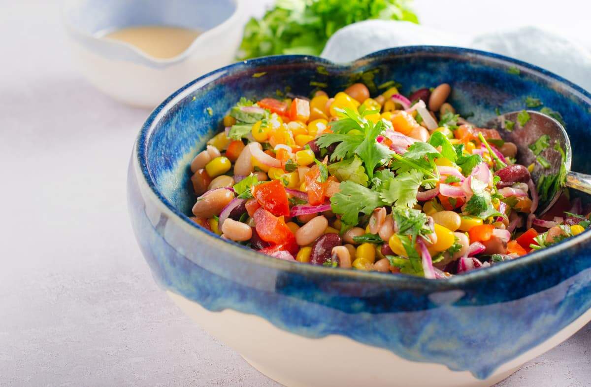 Mixed bean salad in a blue ceramic bowl on a grey surface.