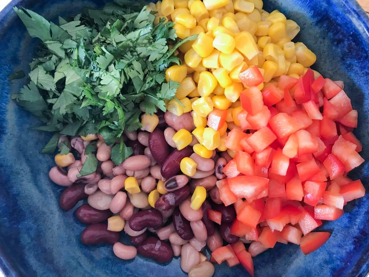 Mixed beans, sweetcorn and chopped coriander in a blue bowl to be mixed as a salad.