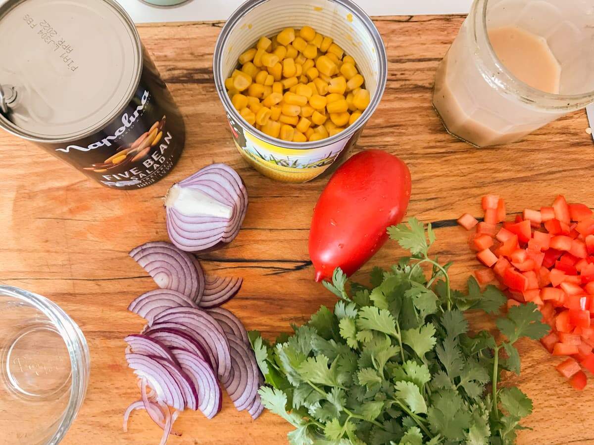 A chopping board full of ingredients, sliced red onion, coriander, diced red pepper, a tomato, sweetcorn and a tin of mixed beans.