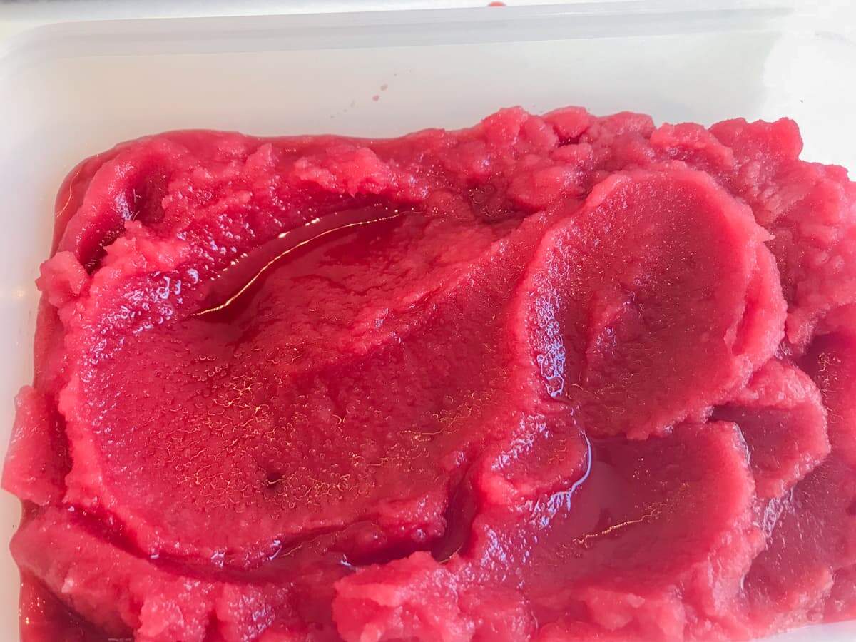 Frozen blood orange sorbet in a plastic tub.