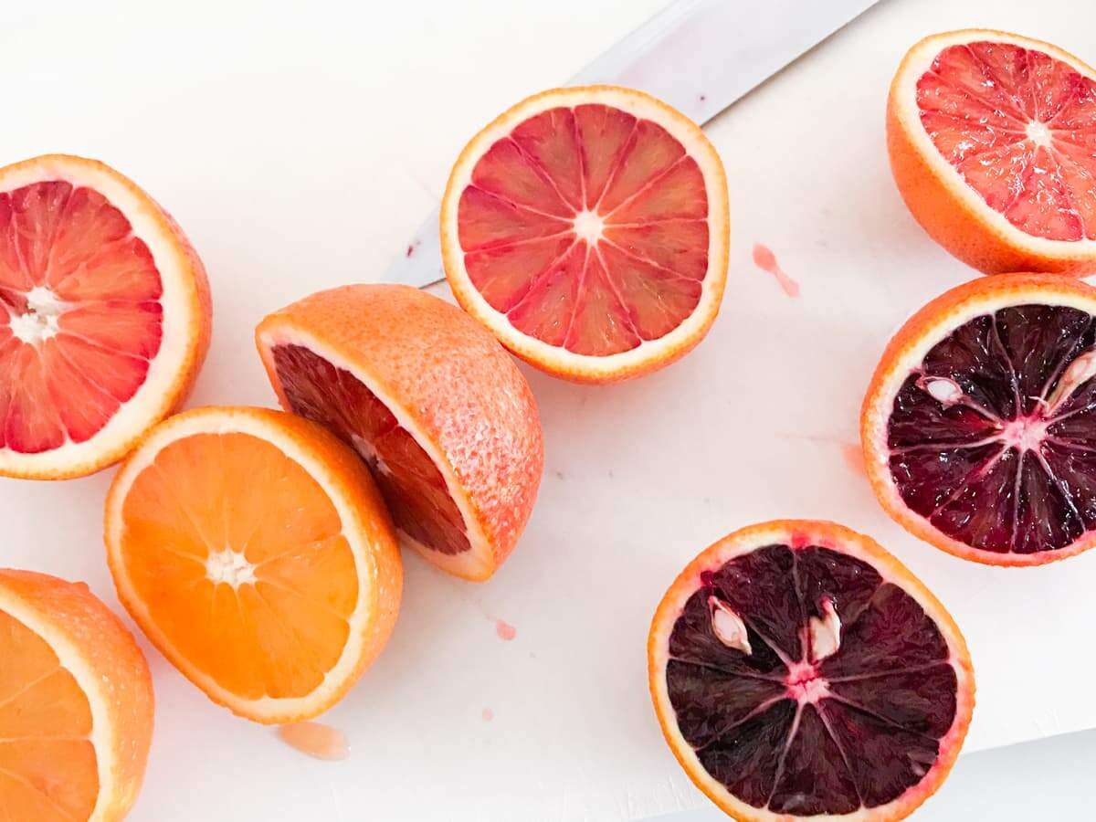 Blood oranges cut in half on a white chopping board showing the beautiful bright colours inside