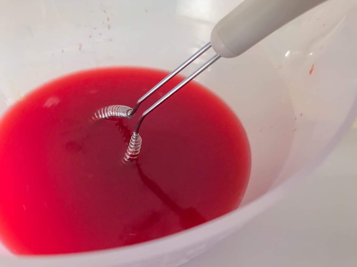 Fresh blood orange juice with a small whisk in a plastic measuring jug.