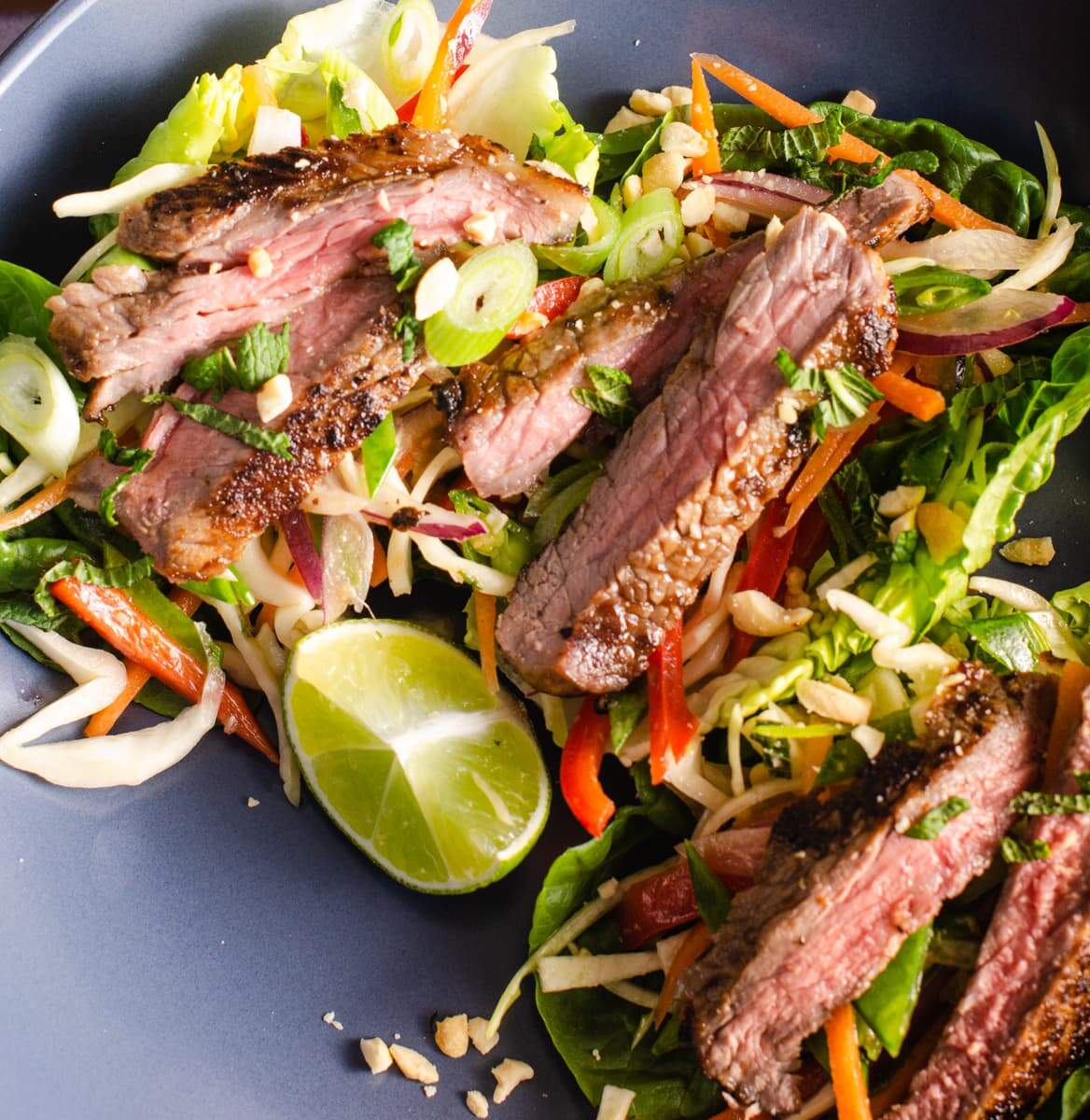 Slices of Asian marinated beef on a colourful slaw base with a wedge of lime.