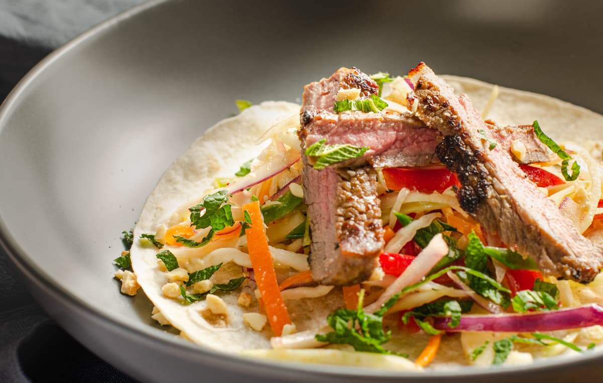 Asian beef salad on a bed of slaw and on a flour tortilla wrap.
