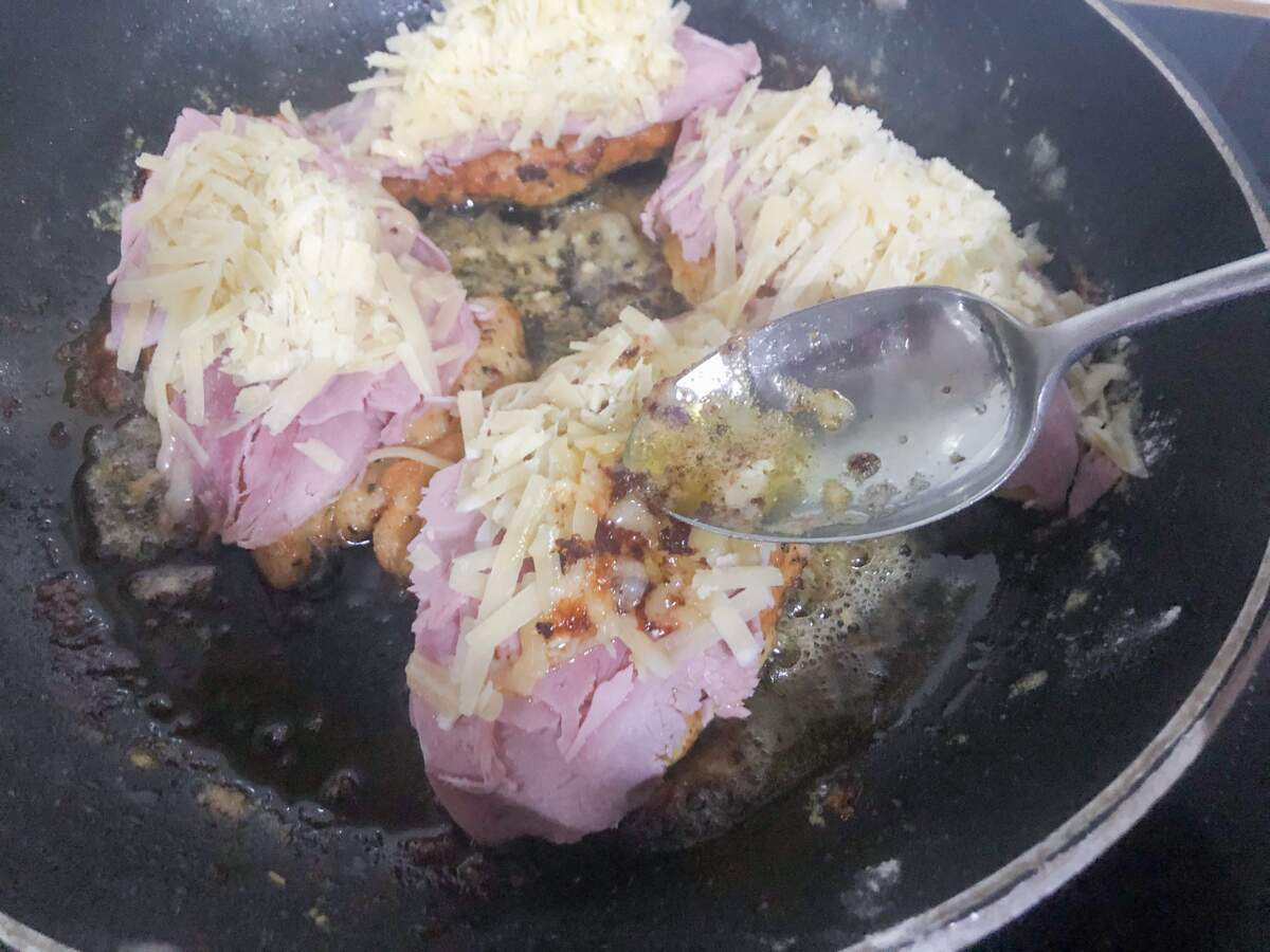 Chicken breast pan frying with ham and cheese over the top.