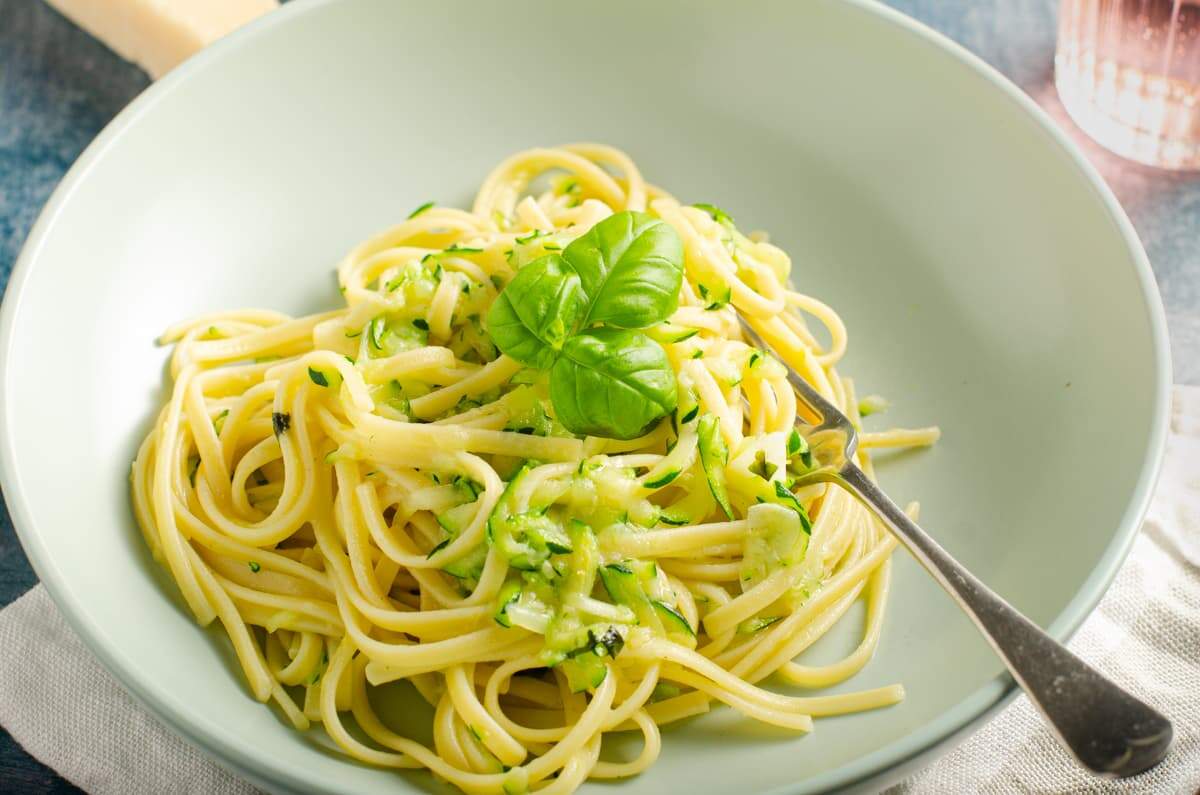 A green bowl of linguine with grated courgette and topped with basil.