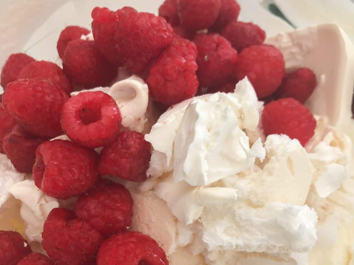 Whipped cream in a bowl, with crushed meringues and fresh raspberries