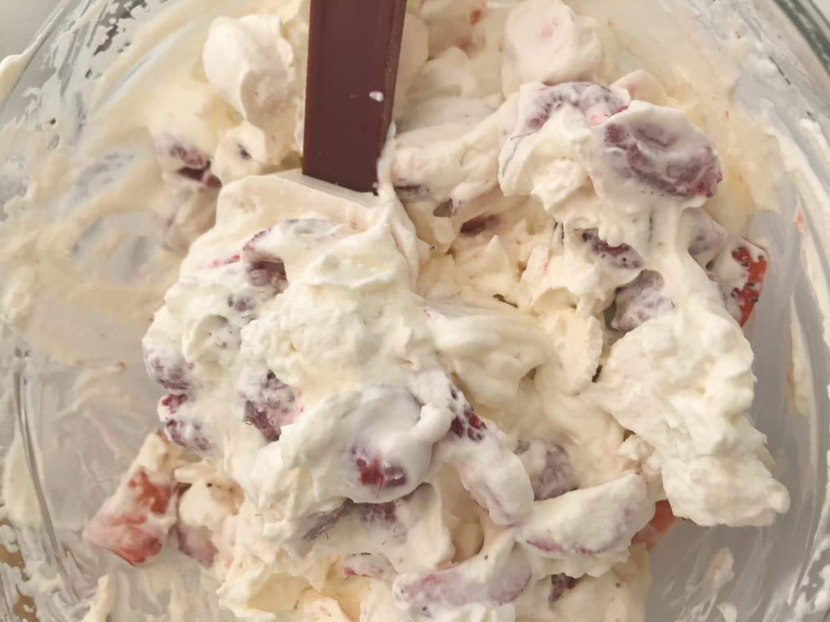 Whipped cream in a bowl, with crushed meringues and fresh raspberries and strawberries