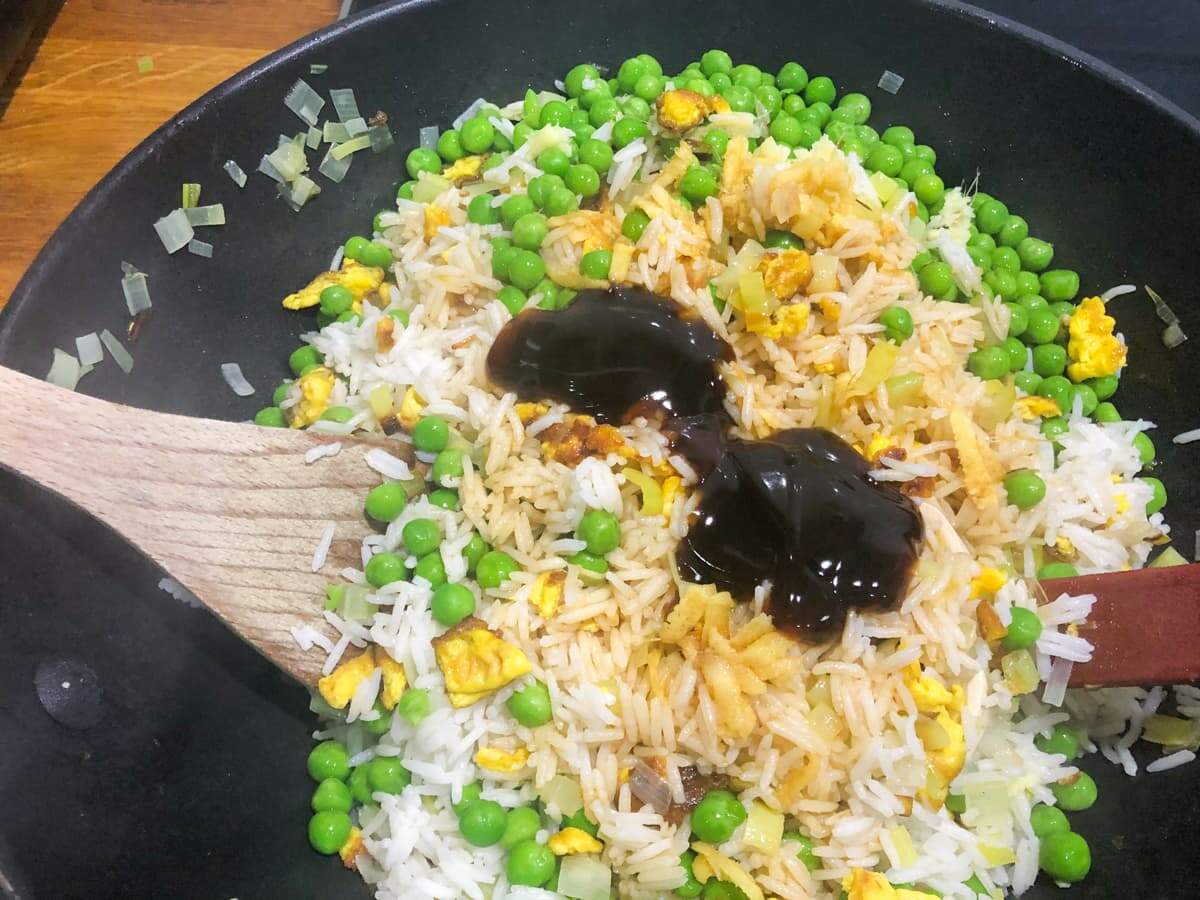 Adding oyster sauce to egg fried rice and tossing in a frying pan.