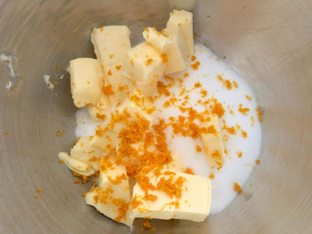 A metal bowl with sugar, cubed butter and orange zest.