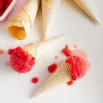Blood orange sorbet in waffle cones from above with melting sorbet on a white marble surface.