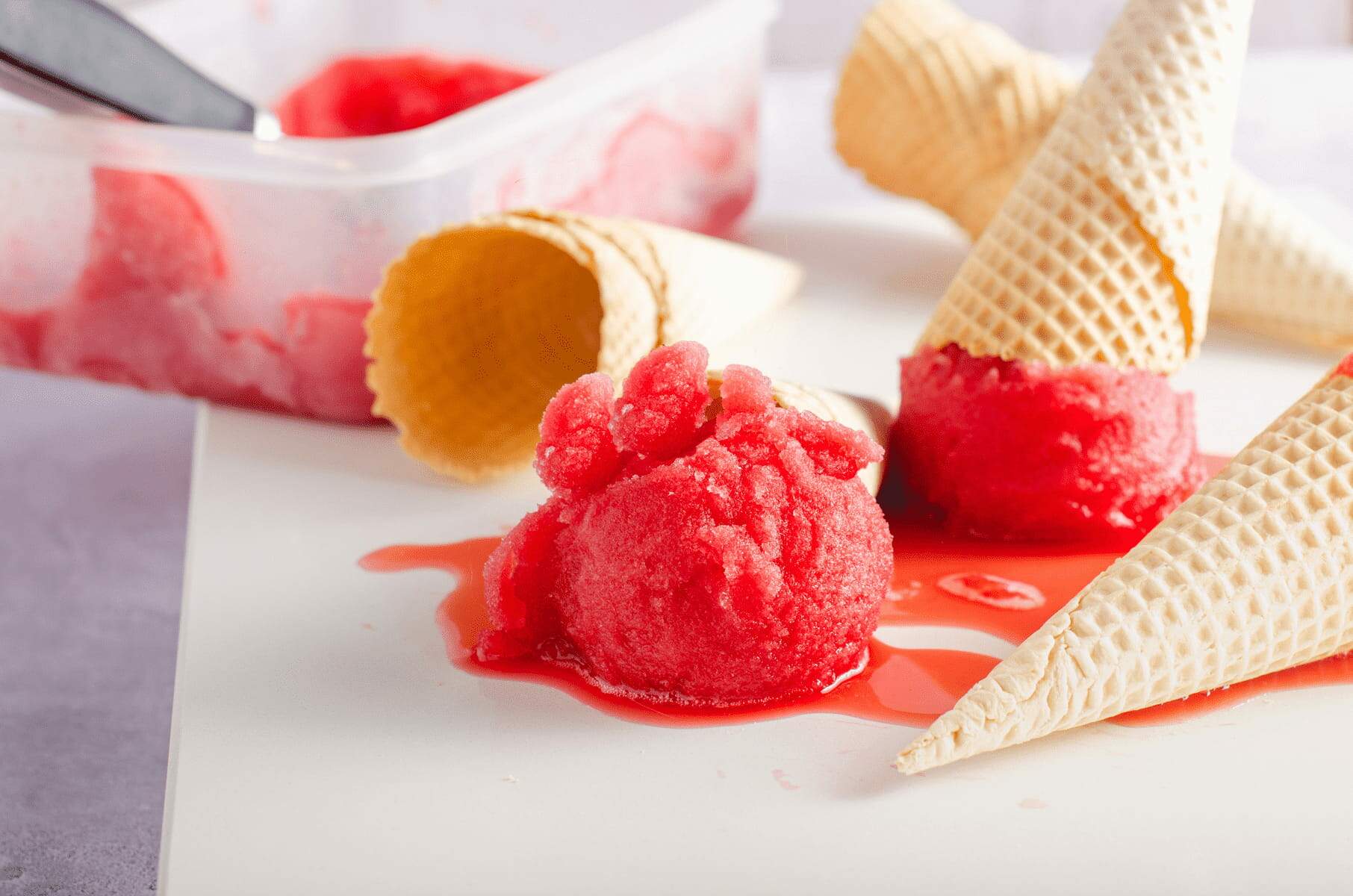 Blood orange sorbet on waffle cones on a white marble surface