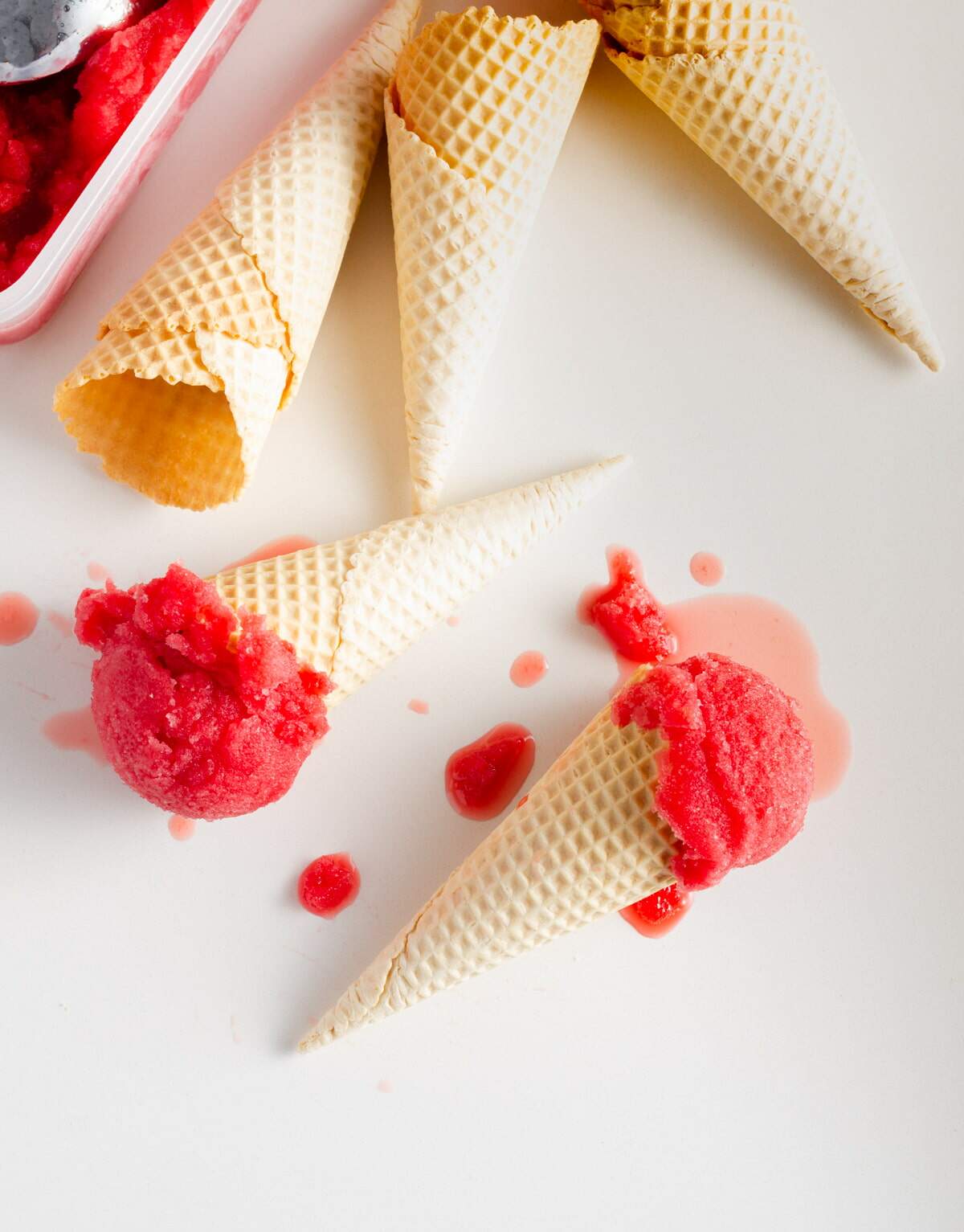 Blood orange sorbet in waffle cones from above with melting sorbet on a white marble surface.
