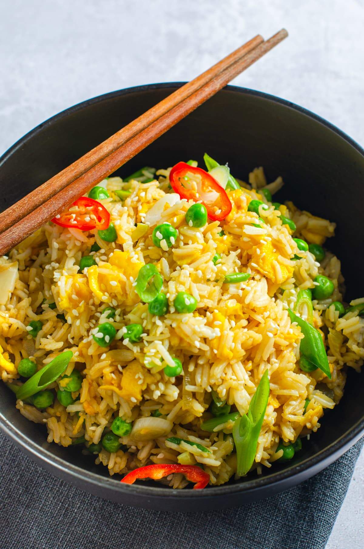 A large black bowl sat on a dark grey linen napkin filled with egg fried rice.