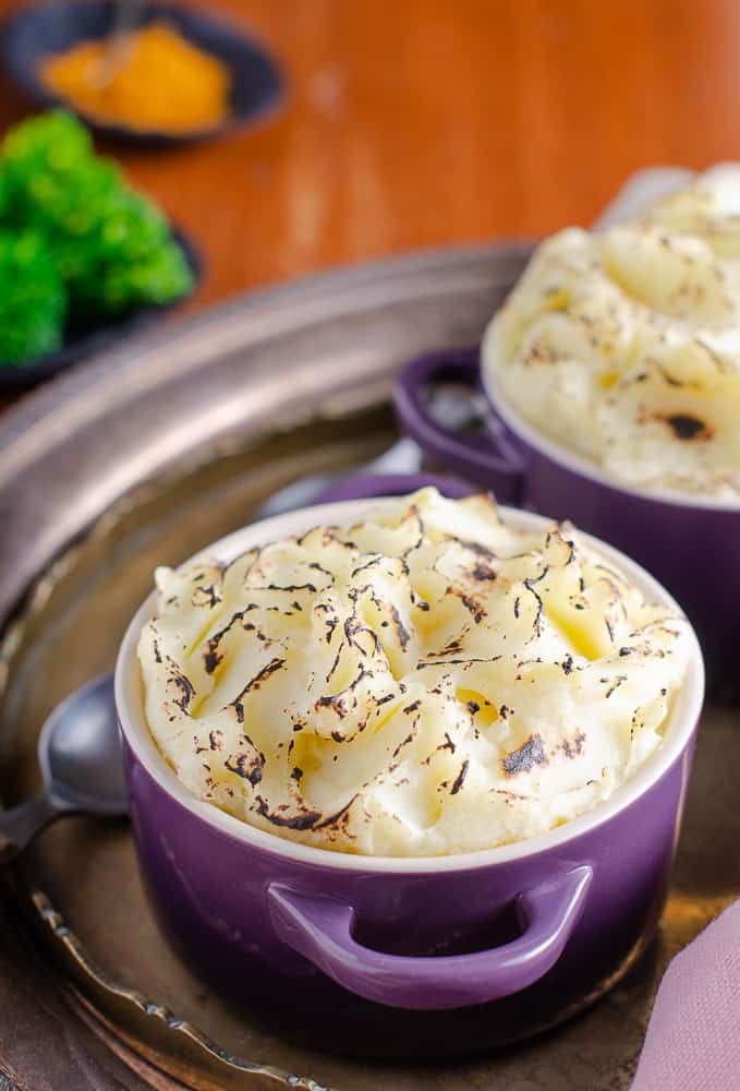 2 portions of Indian cottage pie in Purple dishes with a side of steamed broccoli