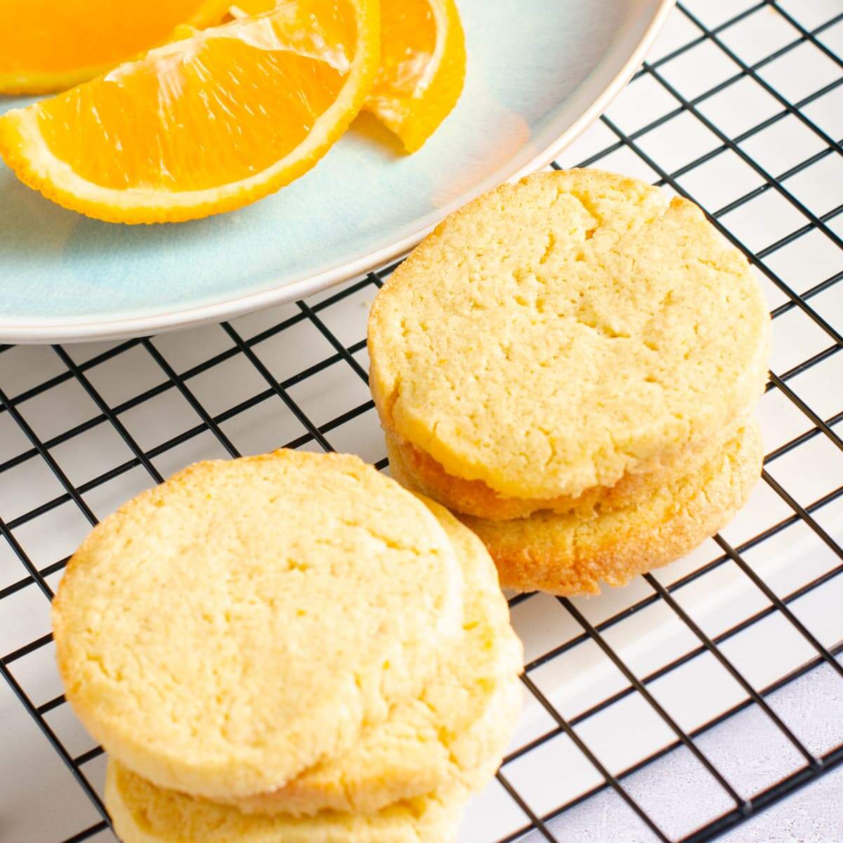 6 orange butter biscuits on a cooling rack and orange segments to the back.