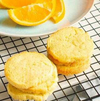 Orange butter cookies on a cooling rack and a sliced orange.