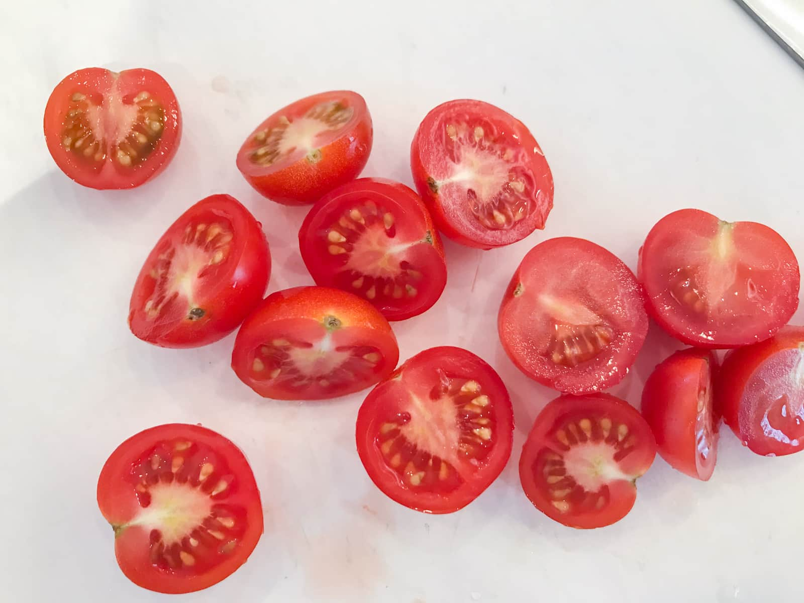 Half sliced cherry tomatoes on a white chopping board.