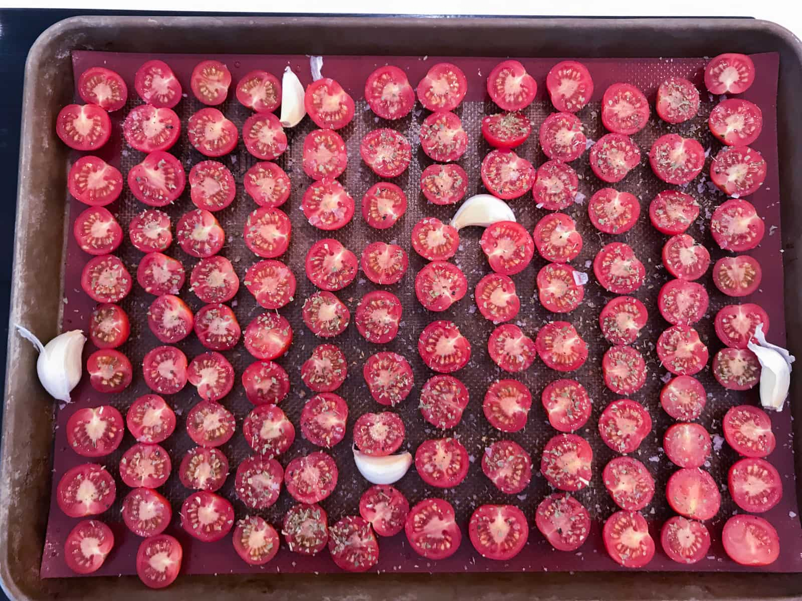 A large tray filled with cherry tomatoes sliced in half and cloves of garlic ready for the oven.