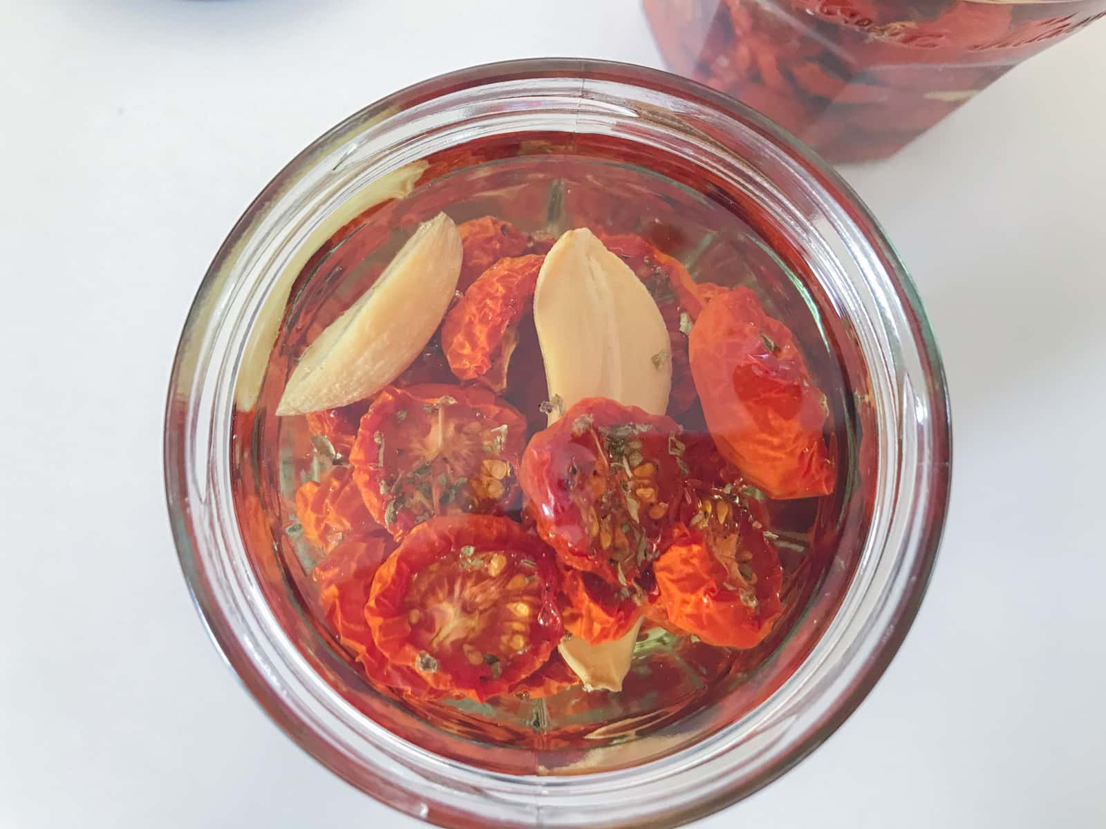 Oven roasted halved cherry tomatoes in a glass jar with confit garlic and topped with olive oil to preserve.