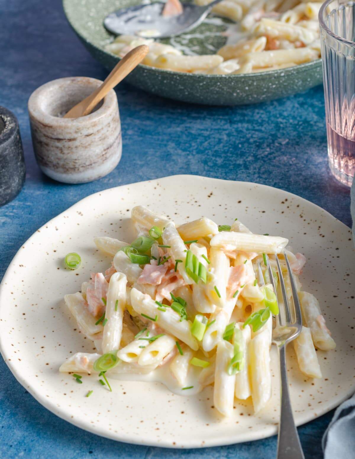 A plate of smoked salmon pasta, with a fork on a blue back drop