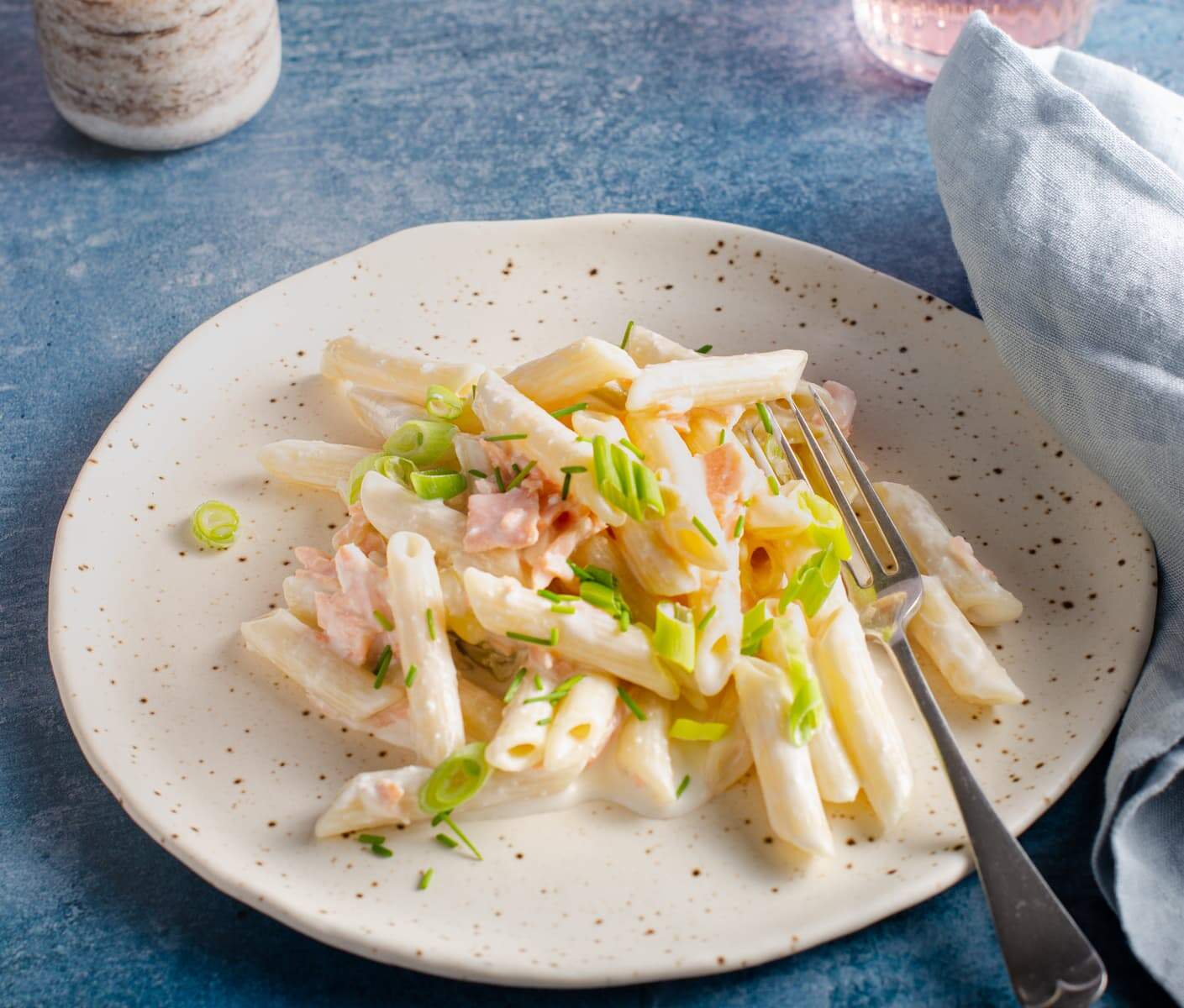 A plate of smoked salmon pasta, with a fork on a blue back drop