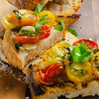 Close up of grilled sourdough bread topped with oven roasted tomatoes and herbs.