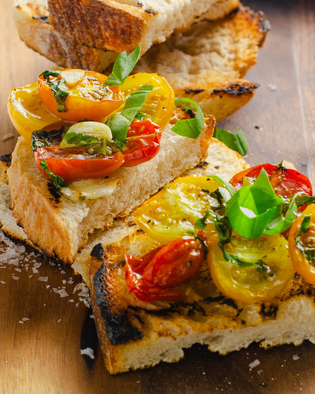 Close up of grilled sourdough bread topped with oven roasted tomatoes and herbs.