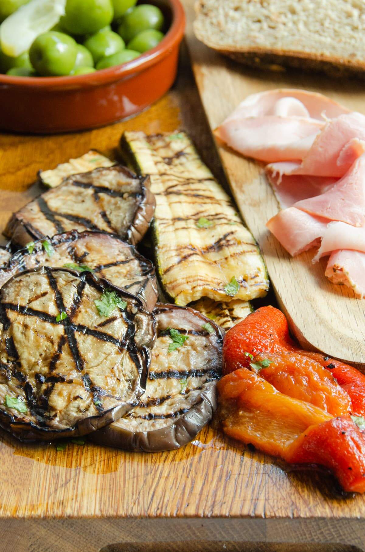 Antipasti board of marinated Mediterranean grilled eggplant, zucchini, and peppers with olives and bread.