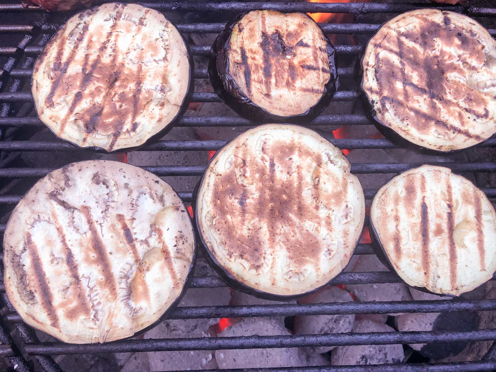 Sliced aubergines (eggplant) on a charcoal bbq grilling.