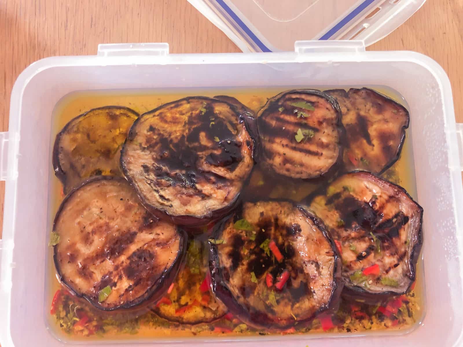 Grilled aubergine in an italian marinade in a plastic lidded container to be stored until needed.