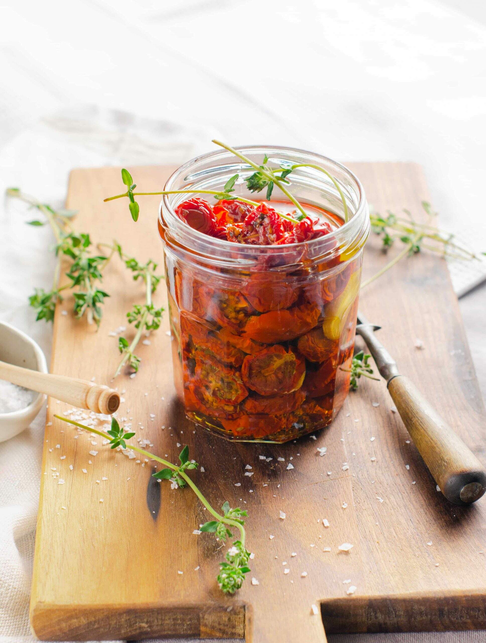 A glass jam jar resused and filled with oven roasted tomatoes and fresh thyme and garlic.