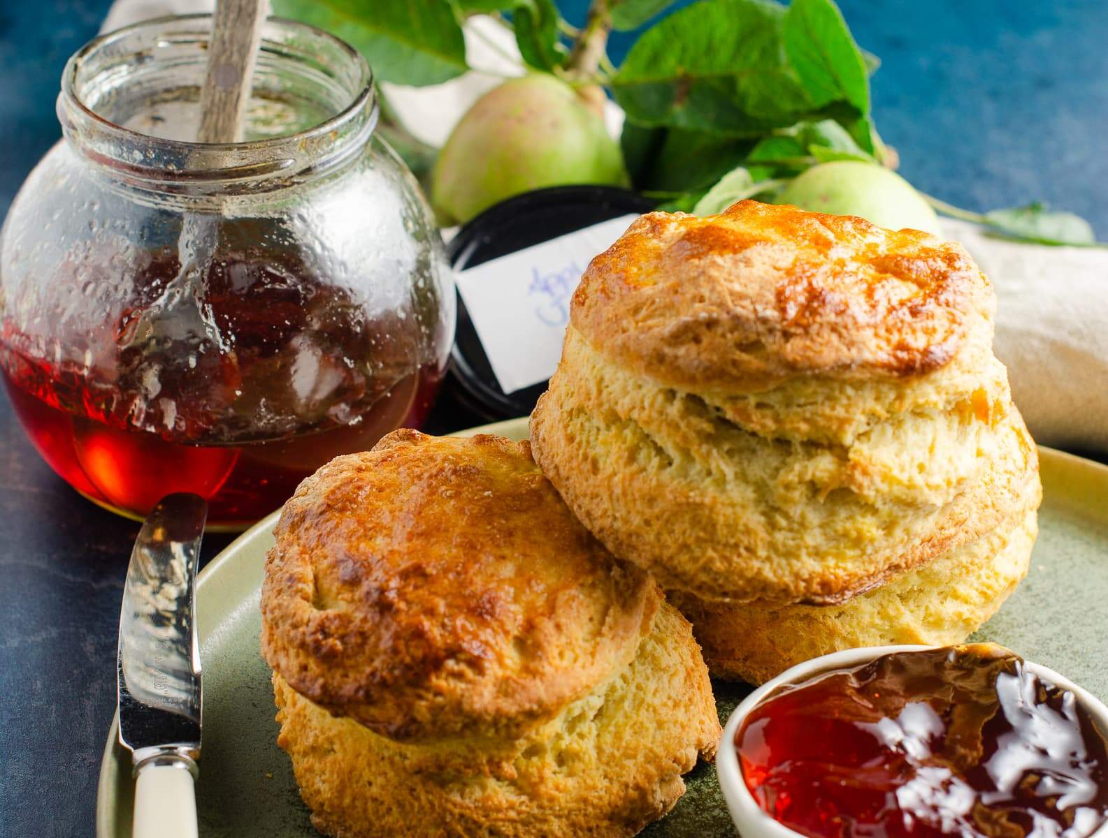 3 fresh scones and apple jelly / jam served on a green plate.