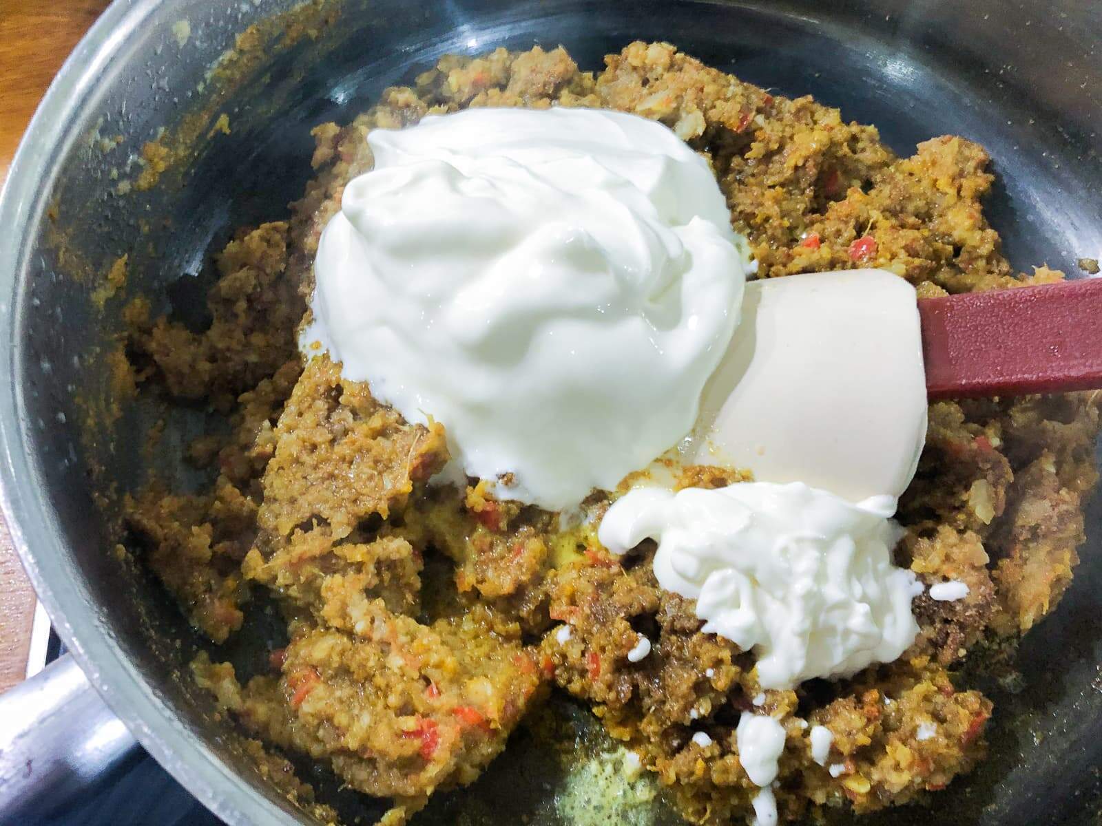 Yogurt being added to a curry spice paste in a frying pan.