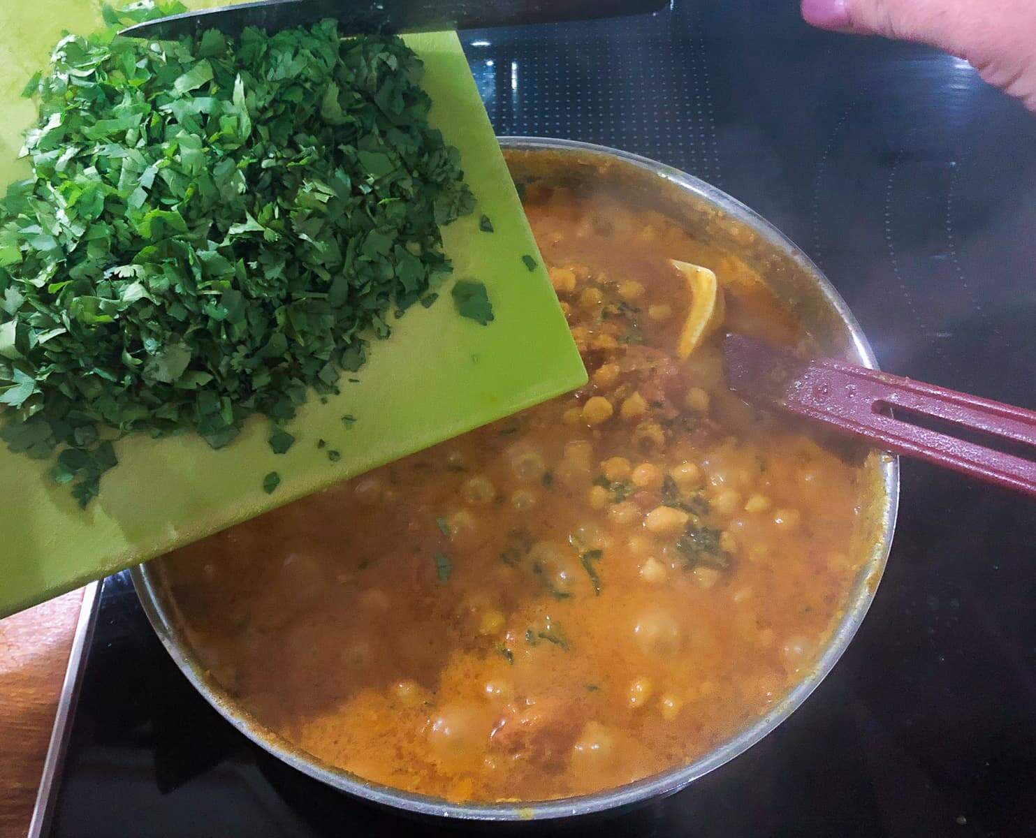 Fresh chopped herbs being added to a pan of simmering curry.