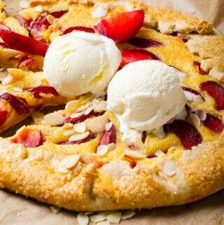 A tart or topped with plums and finished with vanilla ice cream sitting on baking paper.