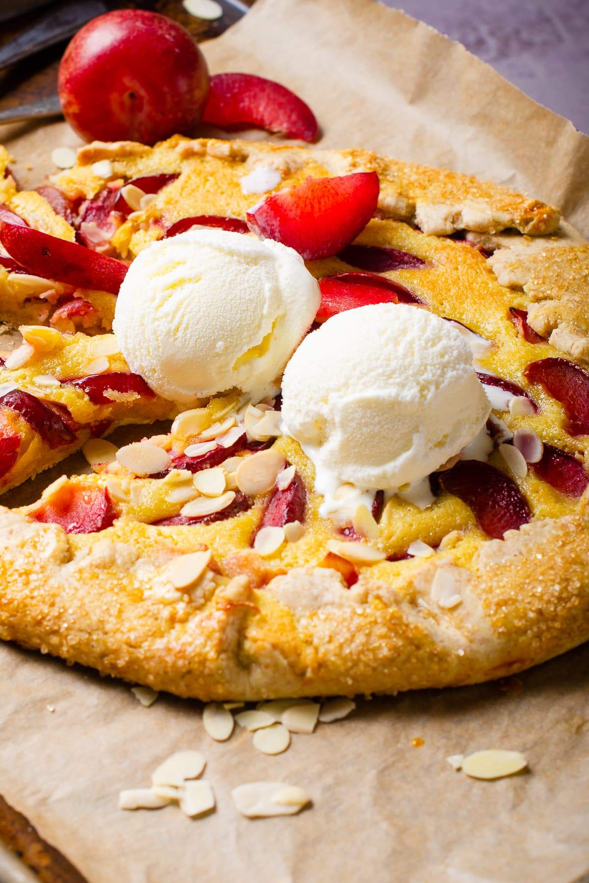 A tart or topped with plums and finished with vanilla ice cream sitting on baking paper.