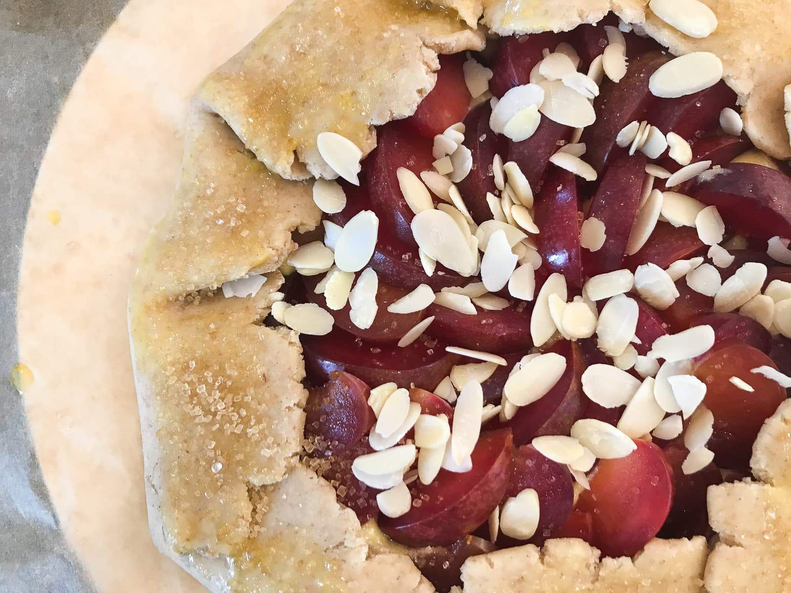A plum tart topped with almonds and demerara sugar ready to be baked.
