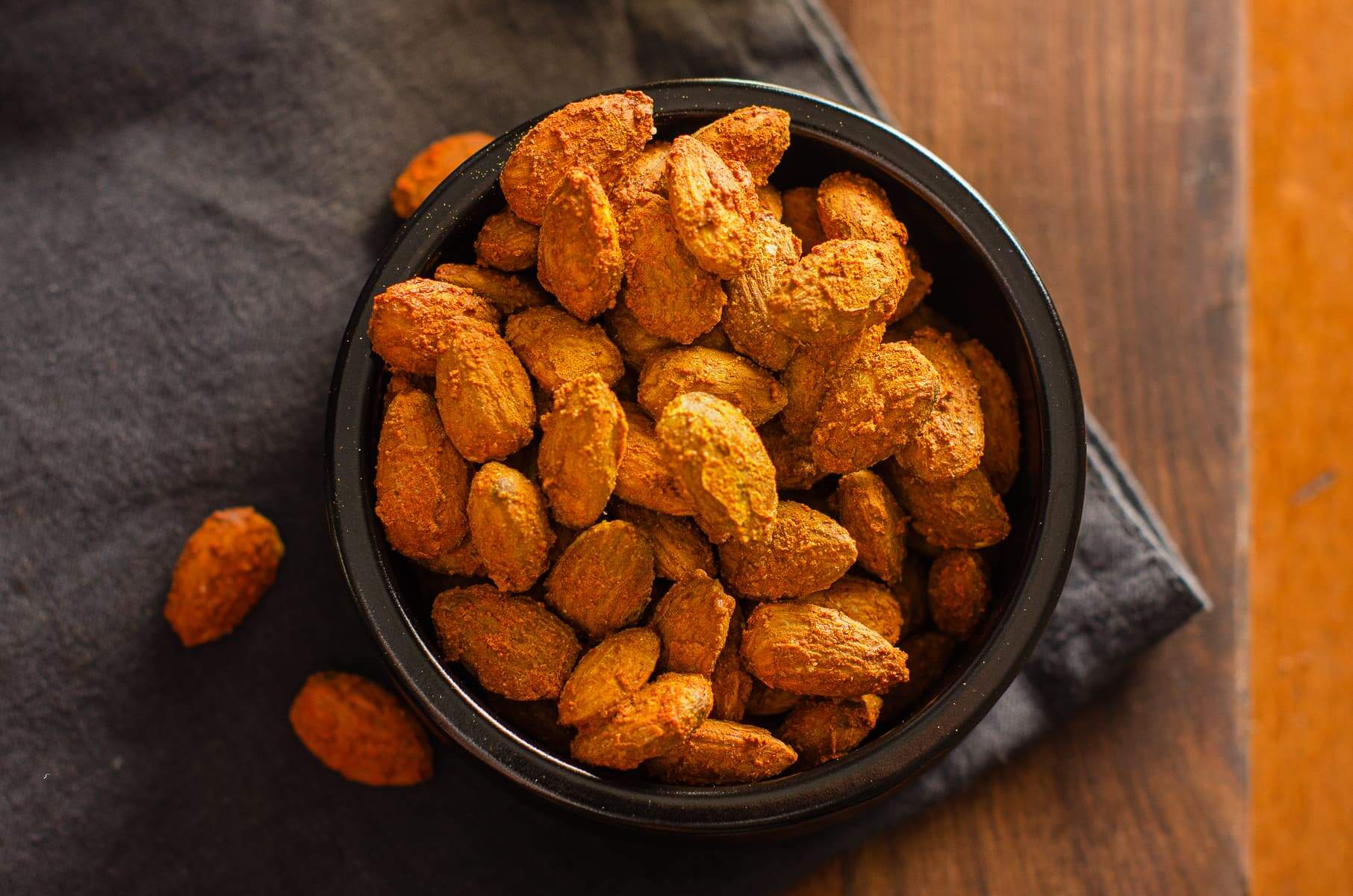 Almonds baked in a spicy coating and served in a black bowl.