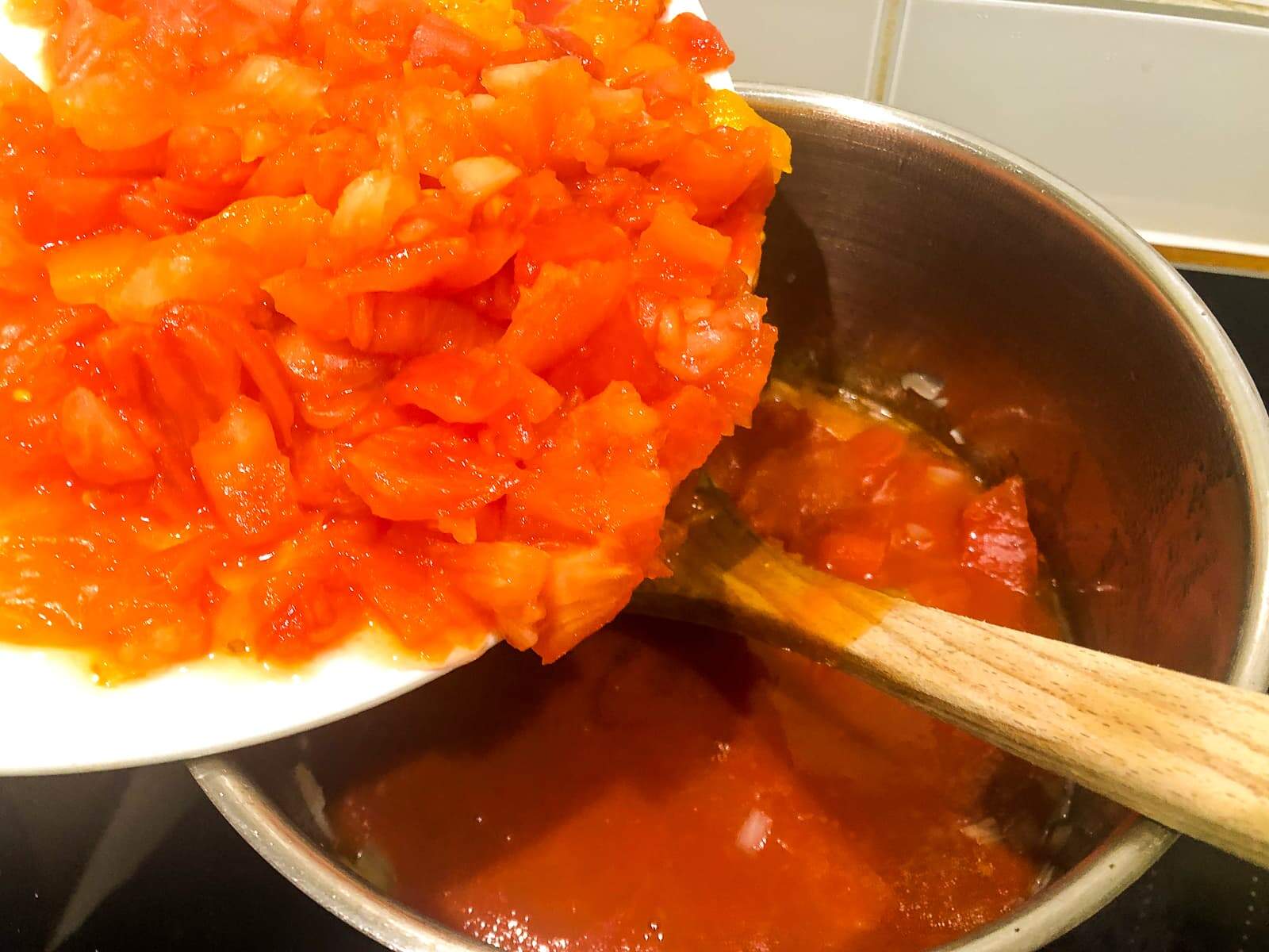 Adding the chopped pulp of tomatoes to the pan after adding the tomato juice.