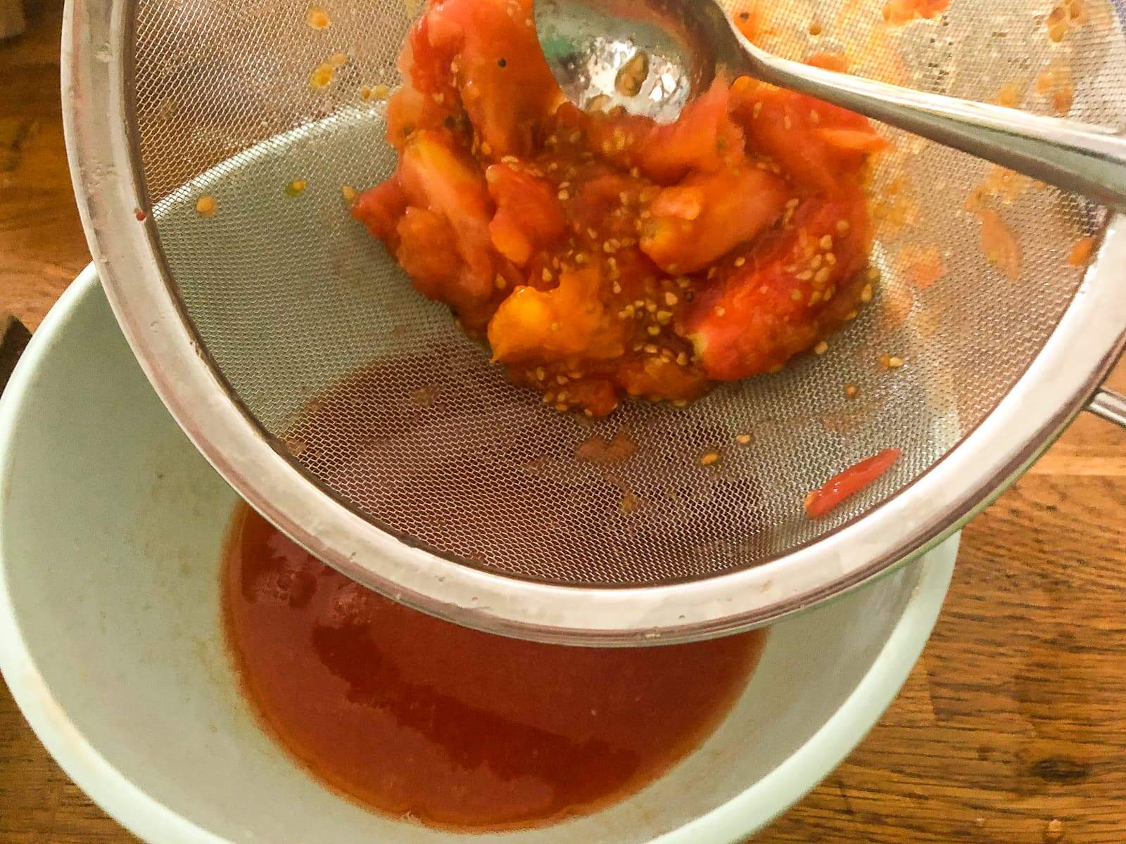 Fresh tomatoes being sieved through a fine strainer to collect the fresh juice.